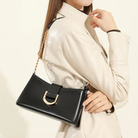 Woman in beige jacket holding black leather shoulder bag with gold chain strap