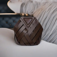 Brown woven leather handbag with triangle flap on white couch, luxury accessory