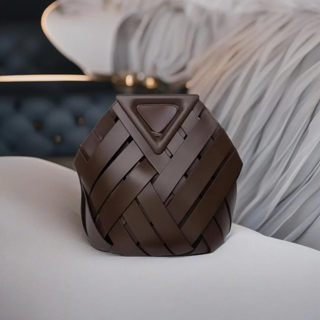 Brown woven leather handbag with triangle flap on white couch, luxury accessory