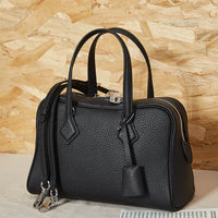 Black leather handbag with silver hardware and top handles on a neutral background
