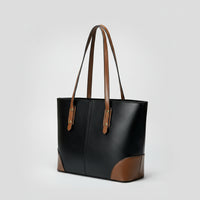 Black leather tote bag with brown handles and accents on a plain gray background