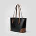 Black leather tote bag with brown handles and accents on a plain gray background