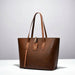 Elegant brown leather tote bag with top handles and tag on a white surface, studio lighting