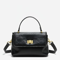 Black leather handbag with gold hardware and top handle on a white background