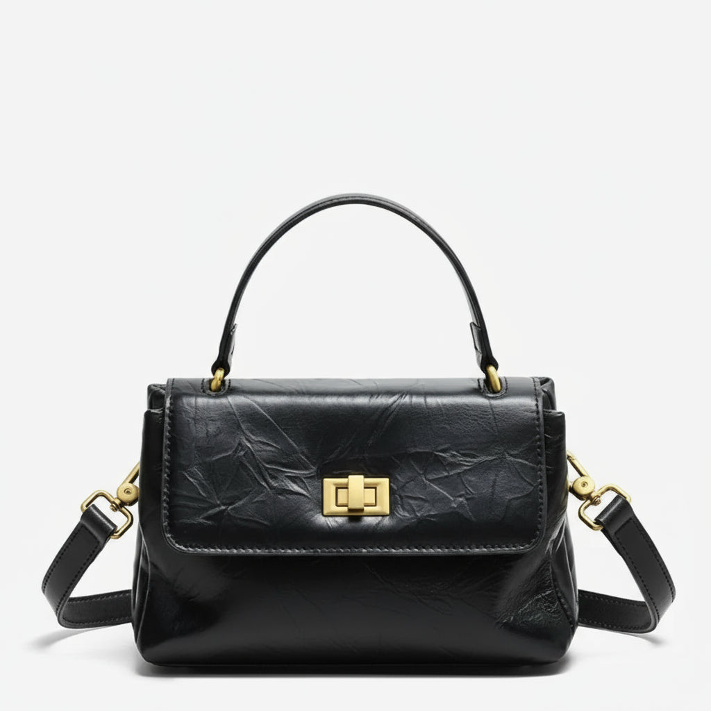 Black leather handbag with gold hardware and top handle on a white background
