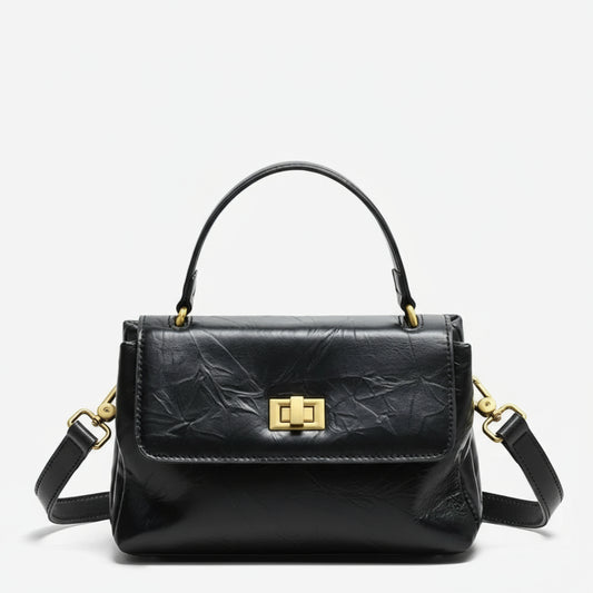 Black leather handbag with gold hardware and top handle on a white background