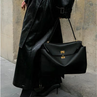 Woman in black leather trench coat holding a large black designer handbag with gold clasps