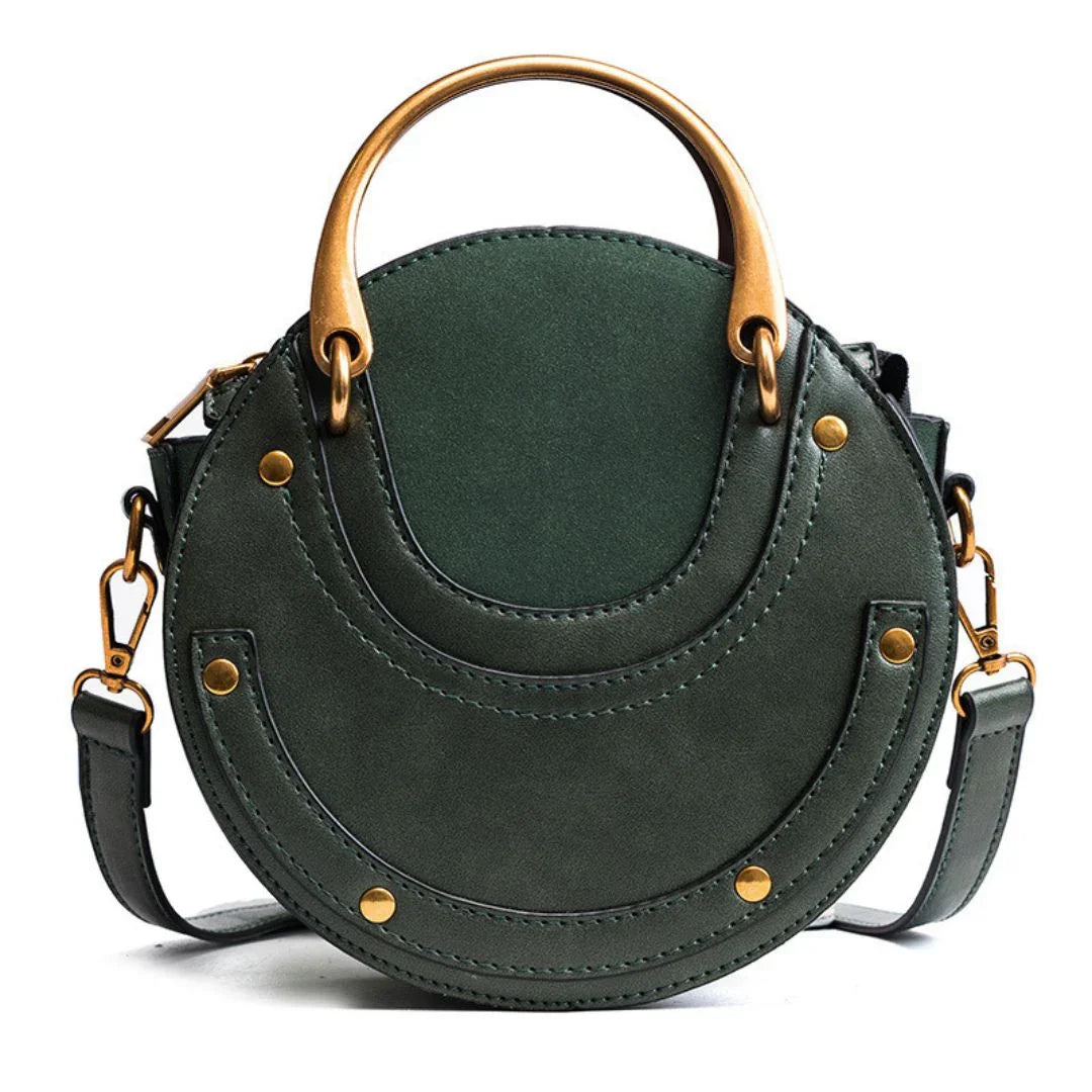 Round green leather handbag with gold rivets and handle on white background