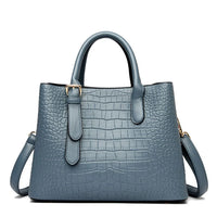 Blue crocodile pattern leather tote bag with top handles and shoulder strap on white background