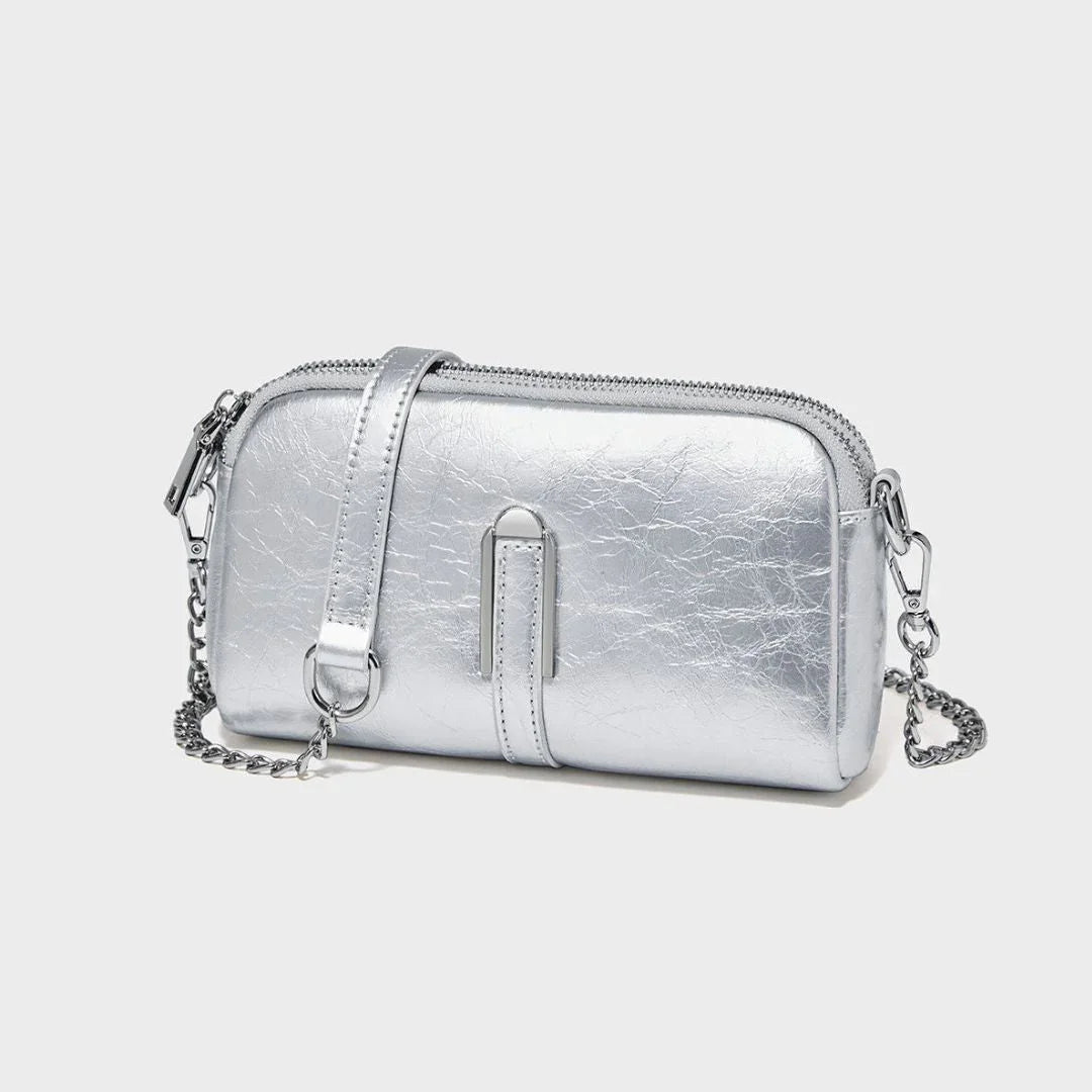 Metallic silver crossbody bag with chain strap and zipper on a plain light background