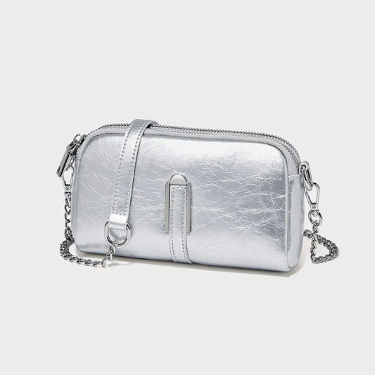 Metallic silver crossbody bag with chain strap and zipper on a plain light background