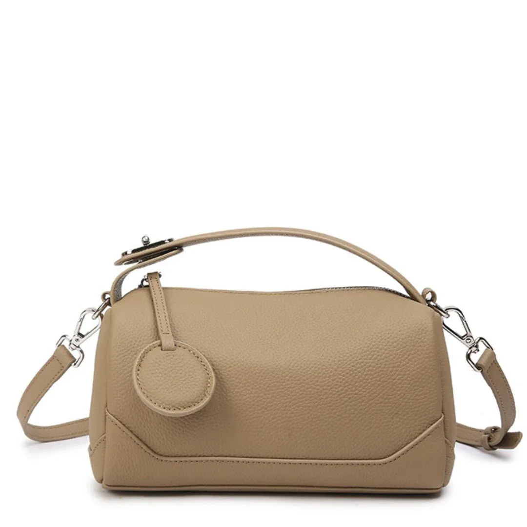 Beige leather handbag with detachable strap and round accent on white background