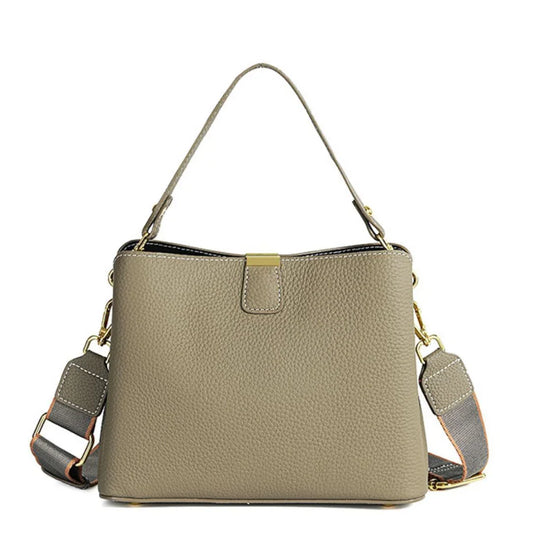 Taupe leather handbag with gold hardware and detachable shoulder strap on white background