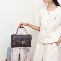 Woman in textured white outfit holding a brown woven leather handbag with gold clasp