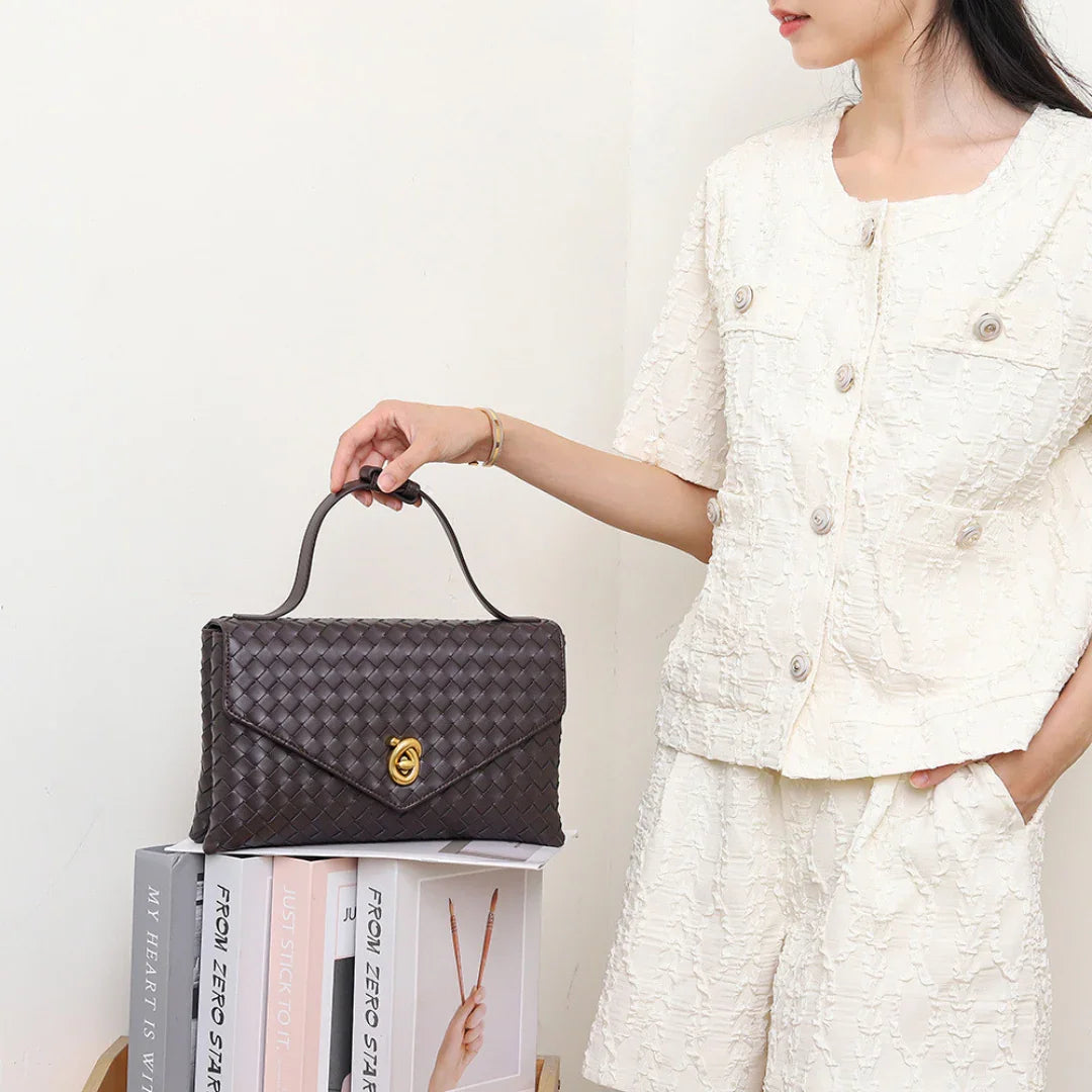 Woman in textured white outfit holding a brown woven leather handbag with gold clasp
