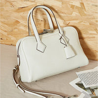 White leather handbag with top handles and a detachable strap on a beige surface
