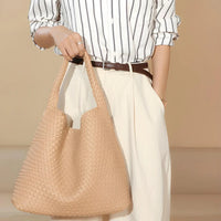 Woman in striped shirt and cream pants holding a large woven beige tote bag