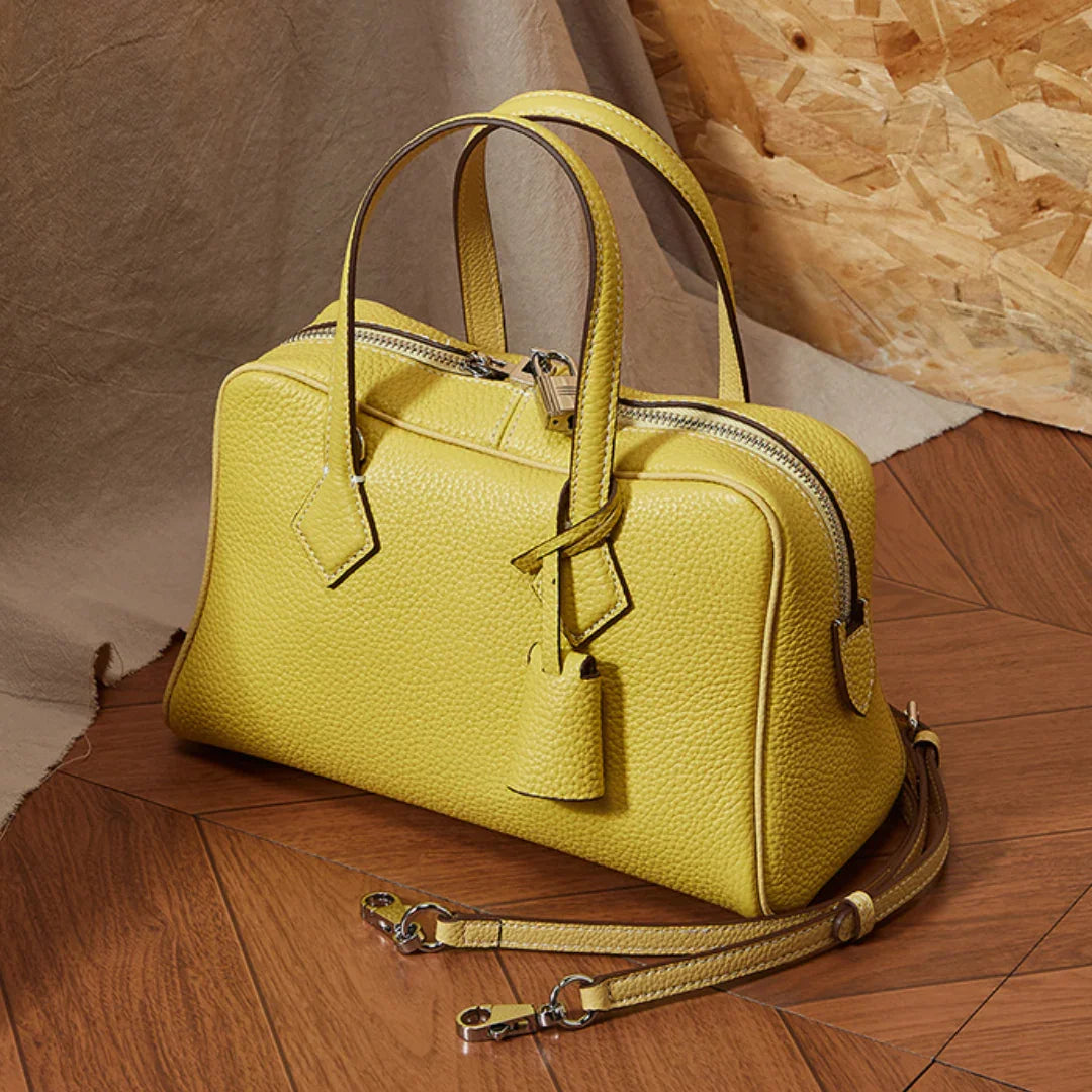 Yellow leather handbag with textured surface and detachable strap on a wooden floor