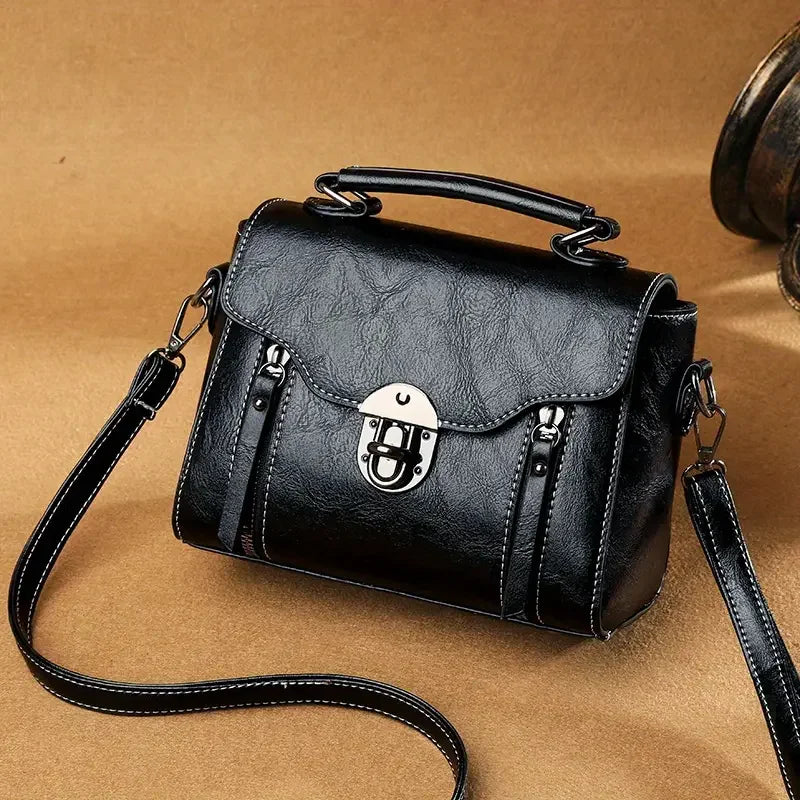 Black leather shoulder bag with top handle and silver clasp on tan background