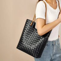Woman wearing woven black leather tote bag with tan handles, white t-shirt, and jeans