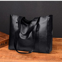Sleek black leather tote bag on wooden table against dark wall