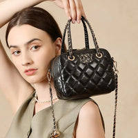 Woman holding quilted black leather handbag with gold chain strap and decorative emblem