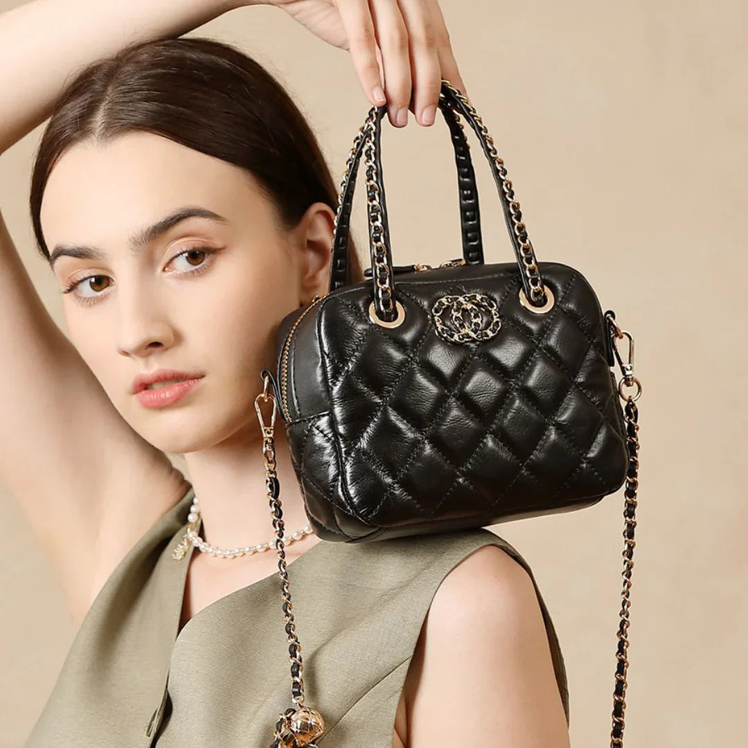 Woman holding quilted black leather handbag with gold chain strap and decorative emblem