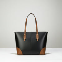 Black leather tote bag with brown handles and corners on a white surface