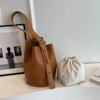 Brown leather bucket bag and beige drawstring pouch on white table, minimalist decor