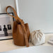 Brown leather bucket bag and beige drawstring pouch on white table, minimalist decor