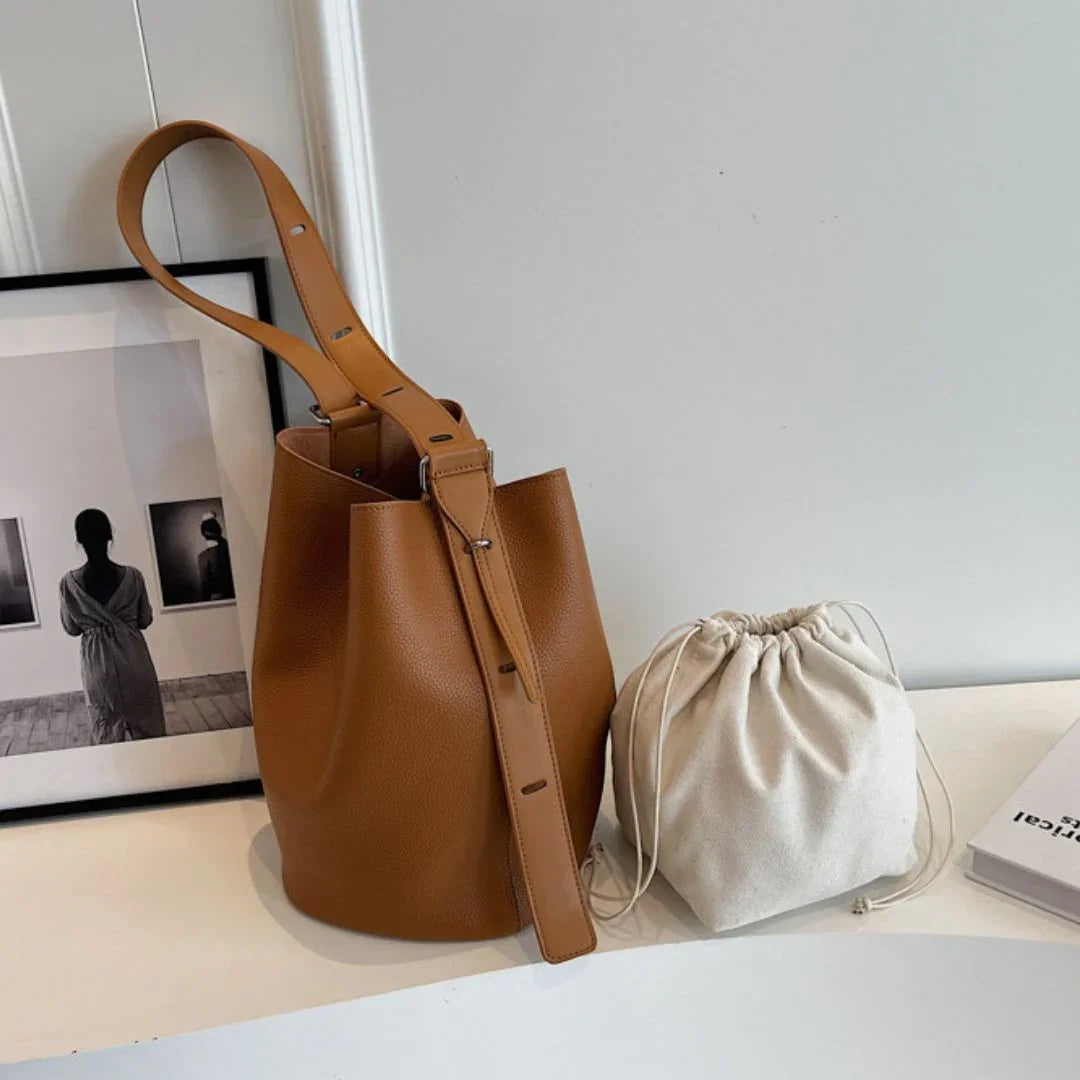 Brown leather bucket bag and beige drawstring pouch on white table, minimalist decor