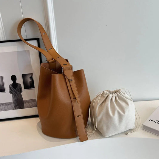 Brown leather bucket bag and beige drawstring pouch on white table, minimalist decor