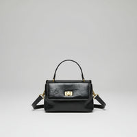 Black leather handbag with top handle, gold clasp, and detachable shoulder strap on white background