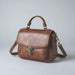 Brown leather satchel handbag with top handle and shoulder strap on plain background