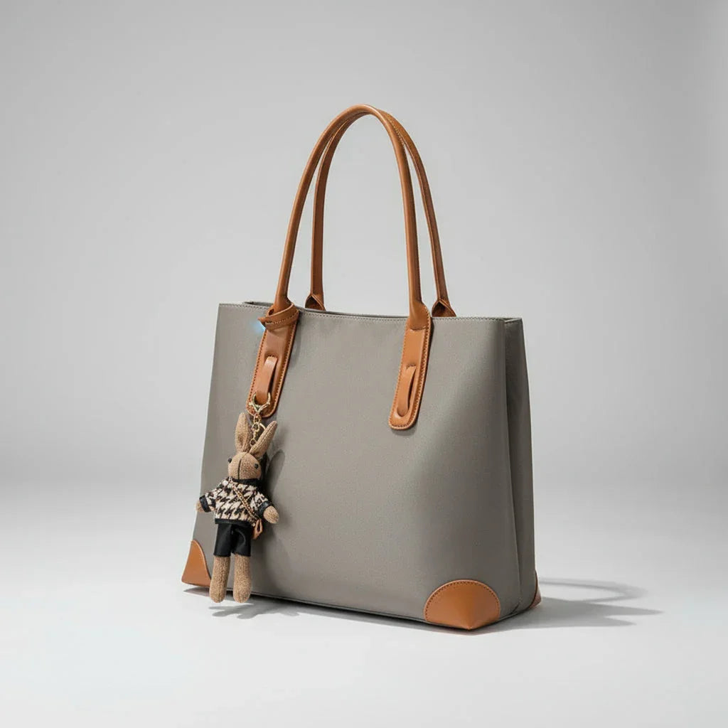 Grey tote bag with brown leather handles and bunny keychain, minimalist background