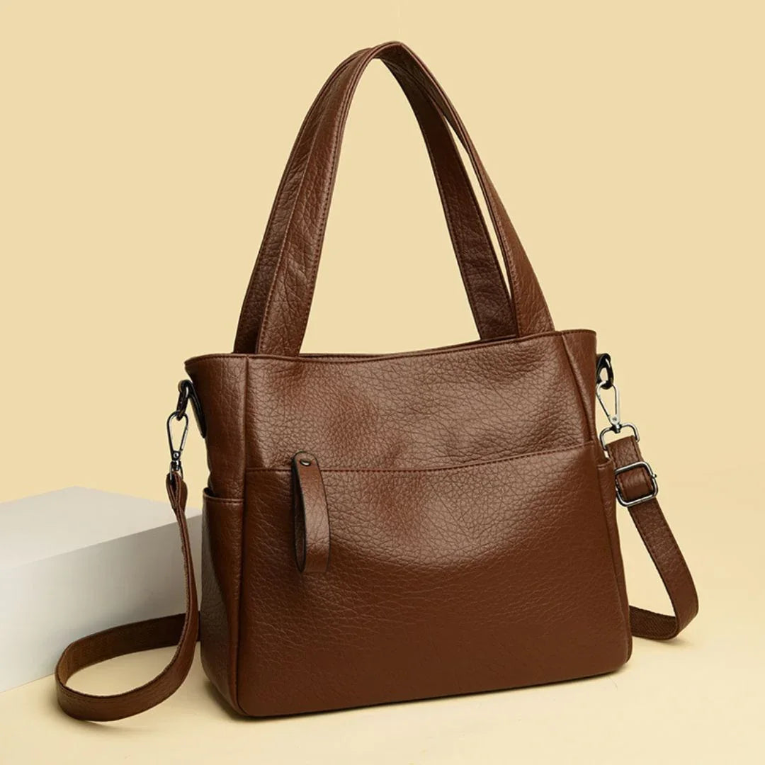 Brown leather handbag with shoulder strap on beige background