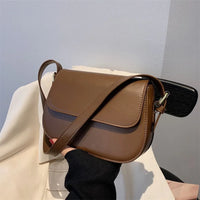 Brown leather crossbody bag with flap closure held by hand indoors
