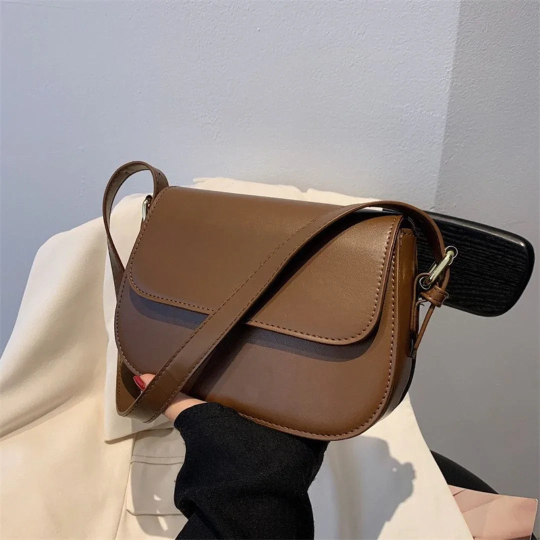 Brown leather crossbody bag with flap closure held by hand indoors
