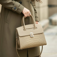 Woman in olive coat holding beige crocodile-embossed leather handbag outdoors