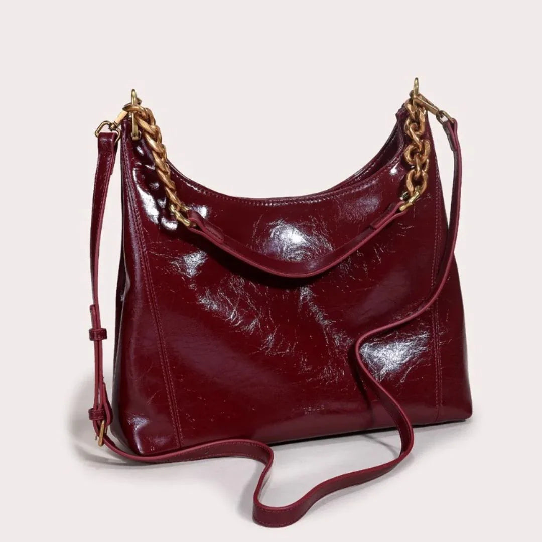Glossy burgundy leather shoulder bag with gold chain strap on light background