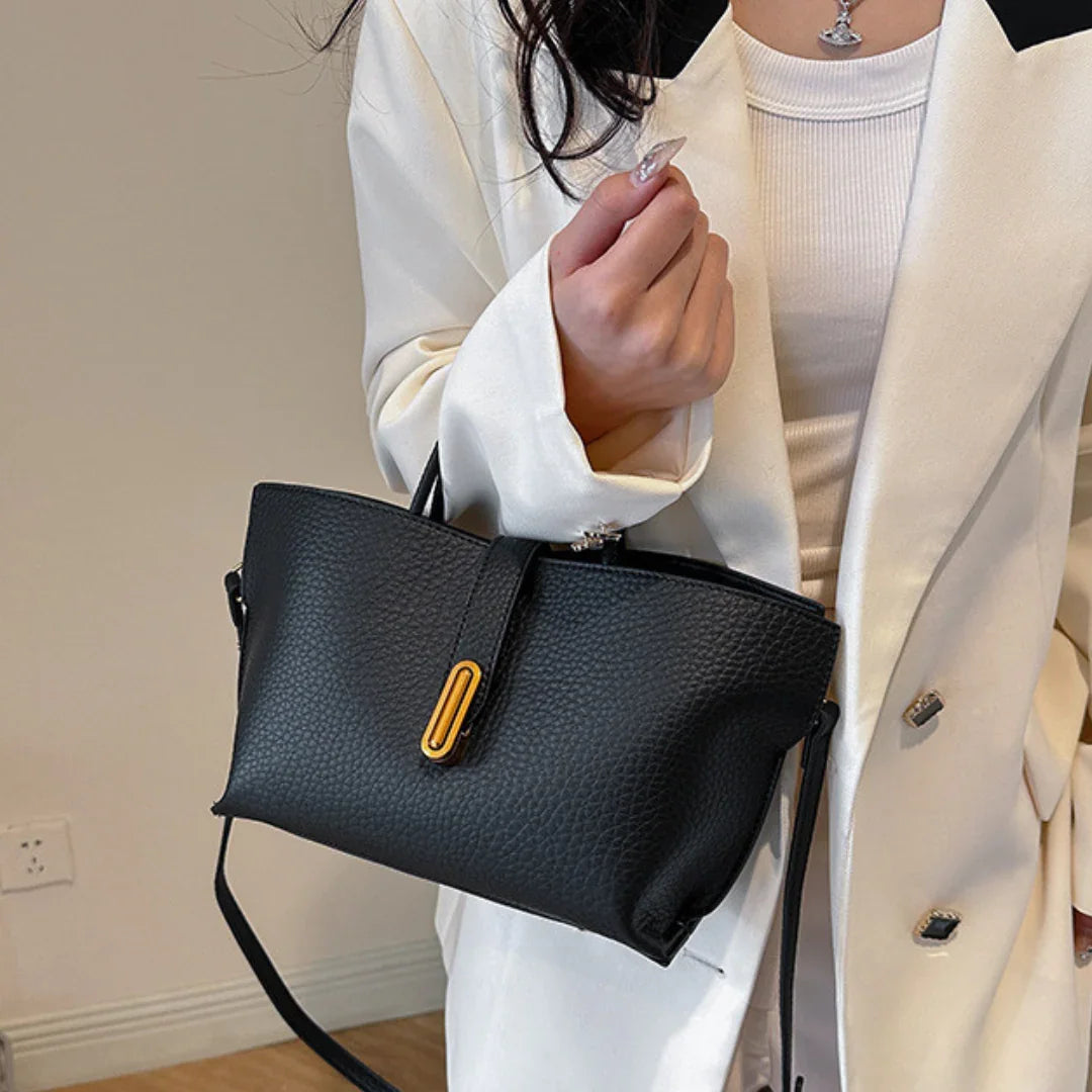 Woman in white blazer holding black textured leather handbag with gold accent