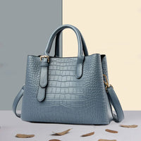 Blue crocodile pattern leather handbag with gold hardware on a two-tone surface