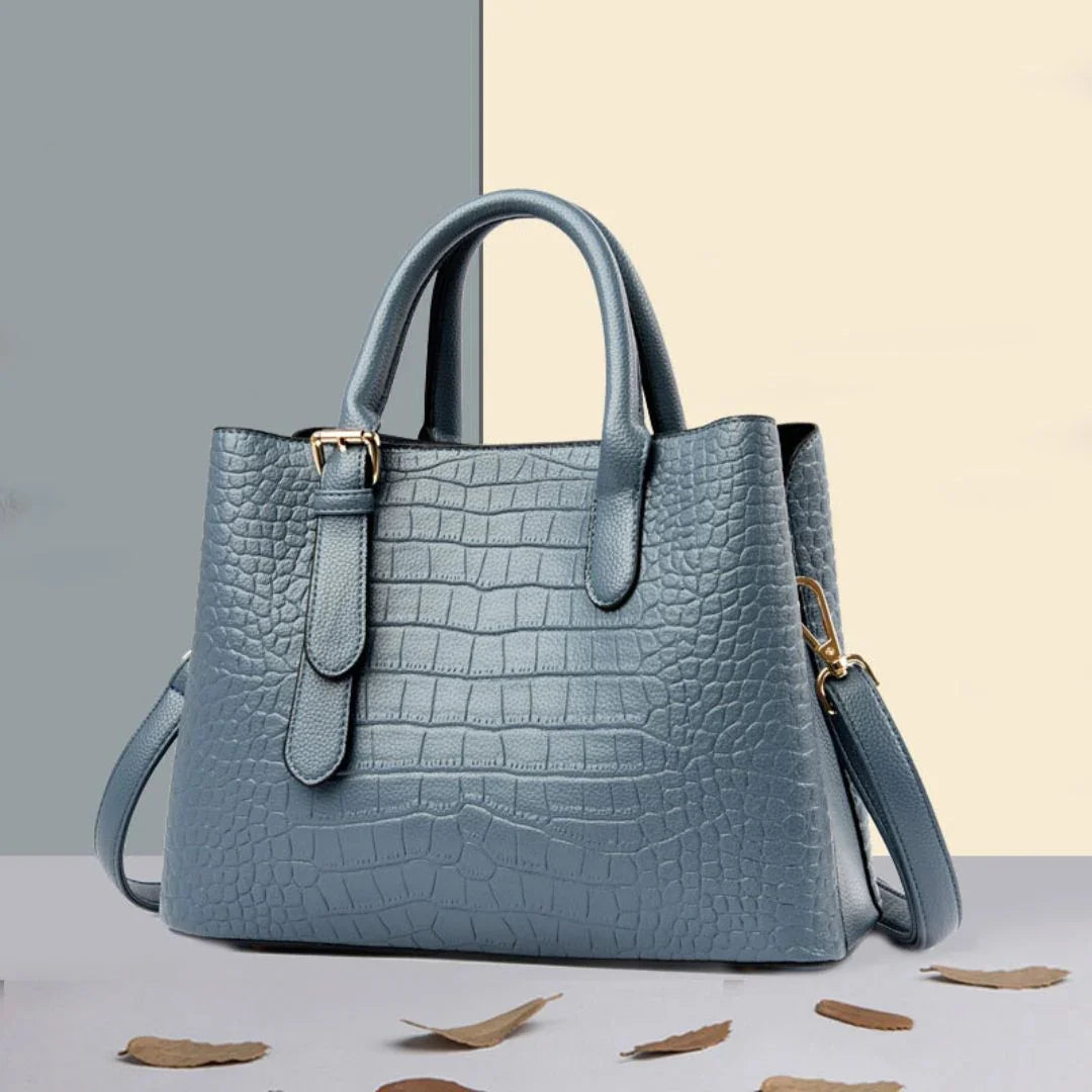 Blue crocodile pattern leather handbag with gold hardware on a two-tone surface