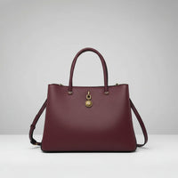 Burgundy leather tote handbag with gold medallion charm and textured finish on white background