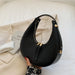 Black crescent hobo bag with gold zipper on a beige coat, minimalist modern style