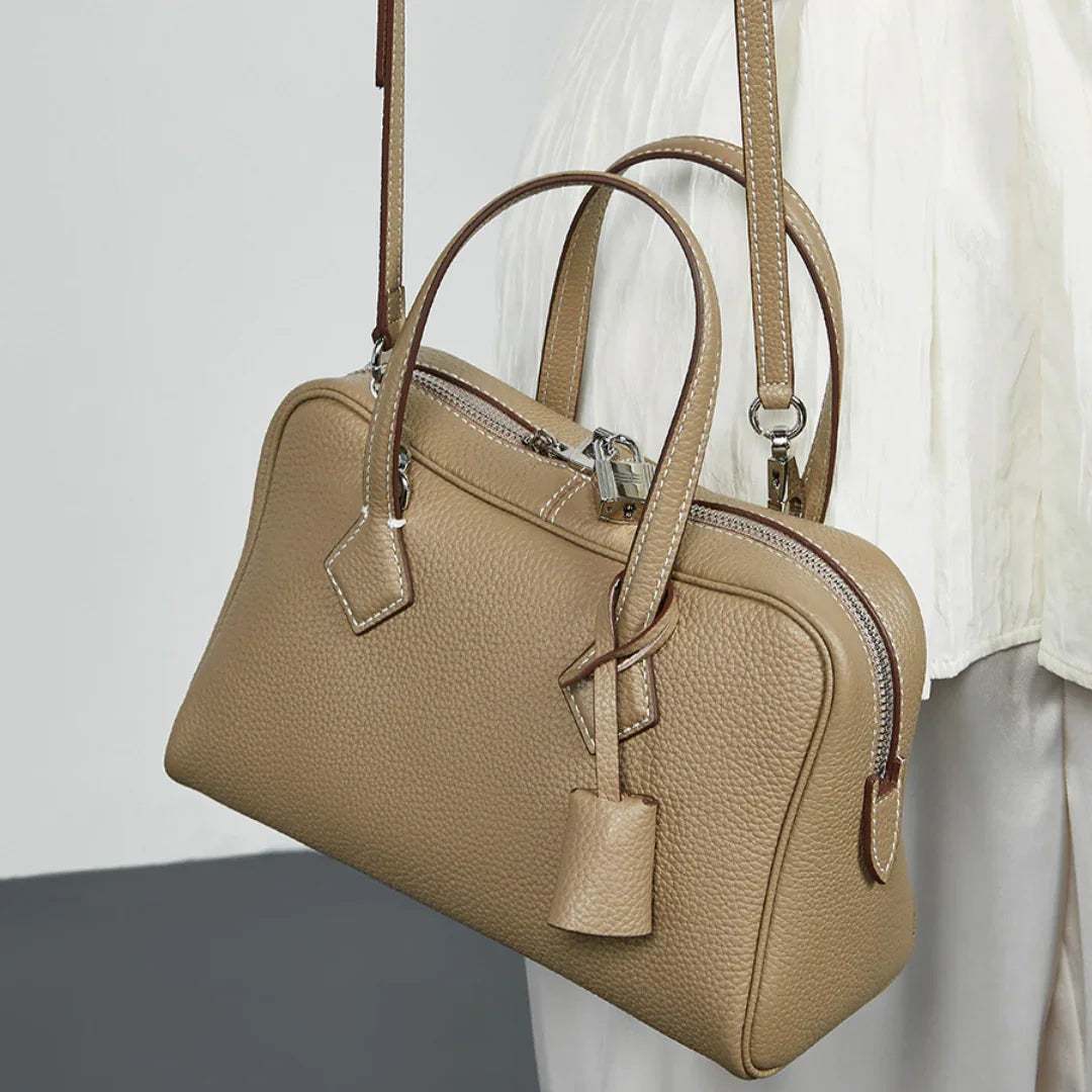 Beige leather top handle bag with shoulder strap and silver hardware, worn over white outfit