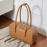 Tan leather handbag with double handles on wooden floor near white wall