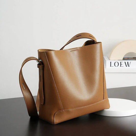 Brown leather tote bag with shoulder strap on dark table, modern minimal decor in background