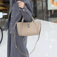 Woman in gray suit holding beige leather handbag with top handle and shoulder strap indoors