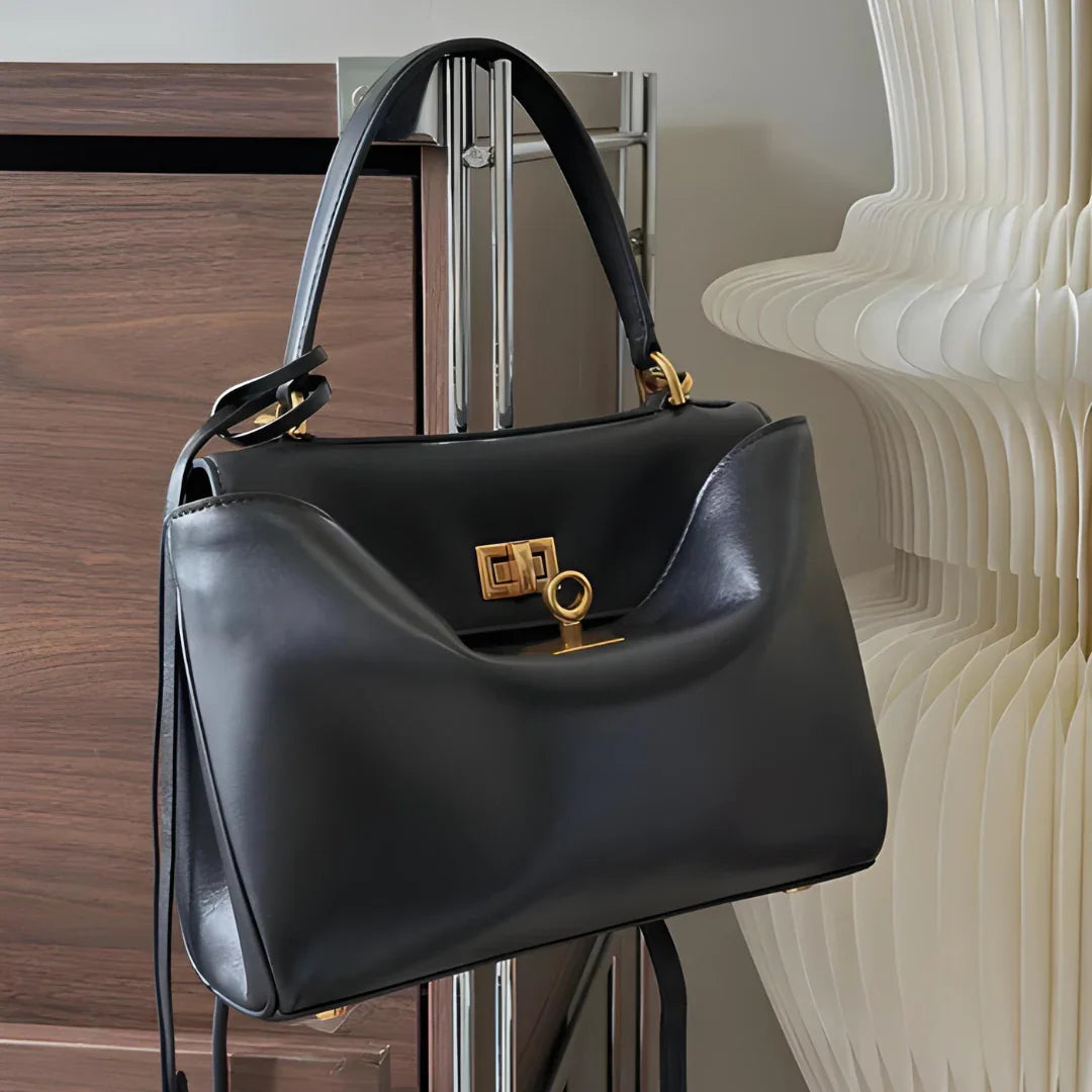 Black leather handbag with gold hardware on modern indoor background